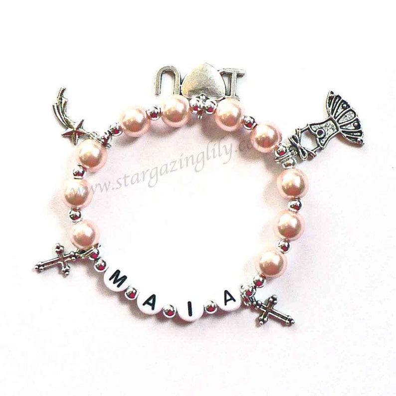 May include: A pink beaded bracelet with silver charms, including a cross, a star, a ballerina, and the letters "NOT" and "MAIA".