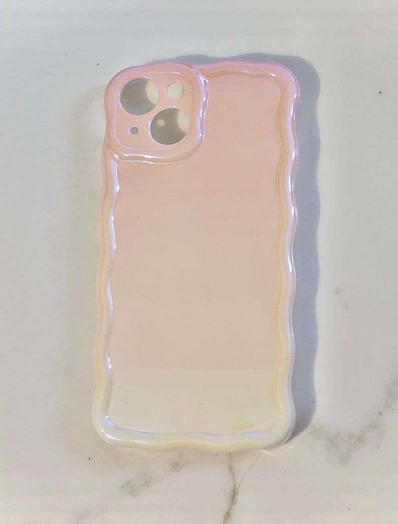May include: A pearlescent phone case with a wavy edge. The case has a gradient of colors, transitioning from a light pink to a soft white. The camera cutouts are visible at the top, and the case is designed to fit a smartphone.