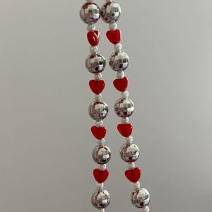 May include: A silver and red beaded phone charm with a disco ball design and heart-shaped beads.