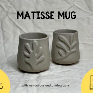 May include: Two ceramic mugs with a Matisse-inspired leaf design. The mugs are a light gray color and have a matte finish. The text "MATISSE MUG" is printed in black at the top of the image.
