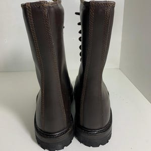 May include: A pair of brown leather boots with a lace-up design. The boots have a tall shaft, a rounded toe, and a thick, textured sole. The stitching is visible along the seams and around the top of the boot.