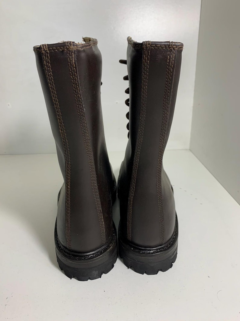 May include: A pair of brown leather boots with a lace-up design. The boots have a tall shaft, a rounded toe, and a thick, textured sole. The stitching is visible along the seams and around the top of the boot.