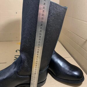 Puede incluir: Botas de cuero negro con un acabado texturizado. Las botas se miden con una regla, mostrando una altura de aproximadamente 38 cm. Tienen un dise&ntilde;o cl&aacute;sico con punta redondeada y suela resistente, adecuadas para diversas actividades.