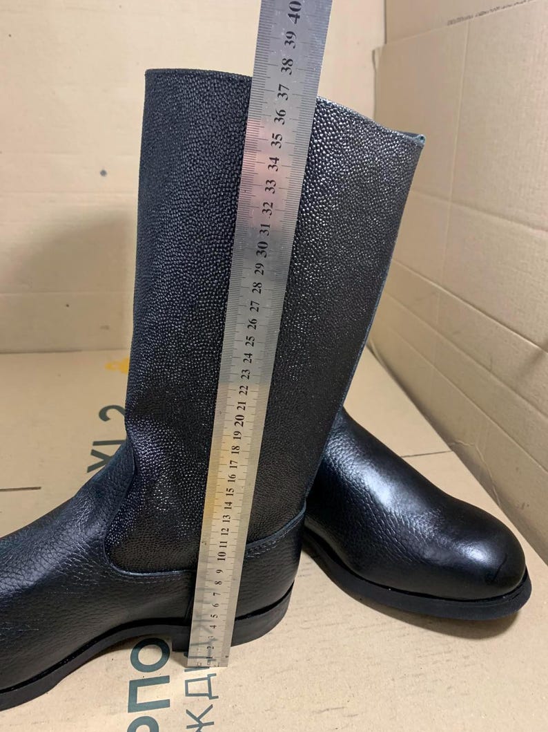 Puede incluir: Botas de cuero negro con un acabado texturizado. Las botas se miden con una regla, mostrando una altura de aproximadamente 38 cm. Tienen un dise&ntilde;o cl&aacute;sico con punta redondeada y suela resistente, adecuadas para diversas actividades.