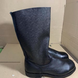 Puede incluir: Botas de cuero negro con superficie texturizada. Las botas tienen ca&ntilde;a alta y suela plana. Fabricadas con un material resistente, son adecuadas para diversas actividades. Altura aproximada: 30 cm.