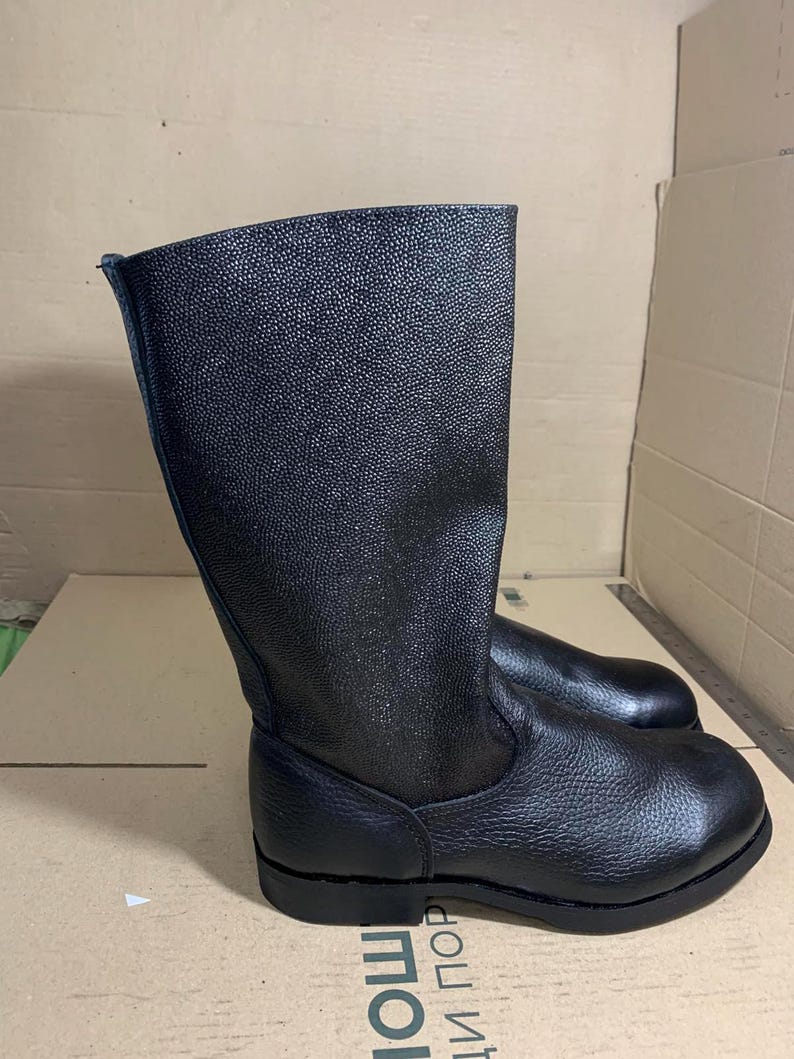Puede incluir: Botas de cuero negro con superficie texturizada. Las botas tienen ca&ntilde;a alta y suela plana. Fabricadas con un material resistente, son adecuadas para diversas actividades. Altura aproximada: 30 cm.