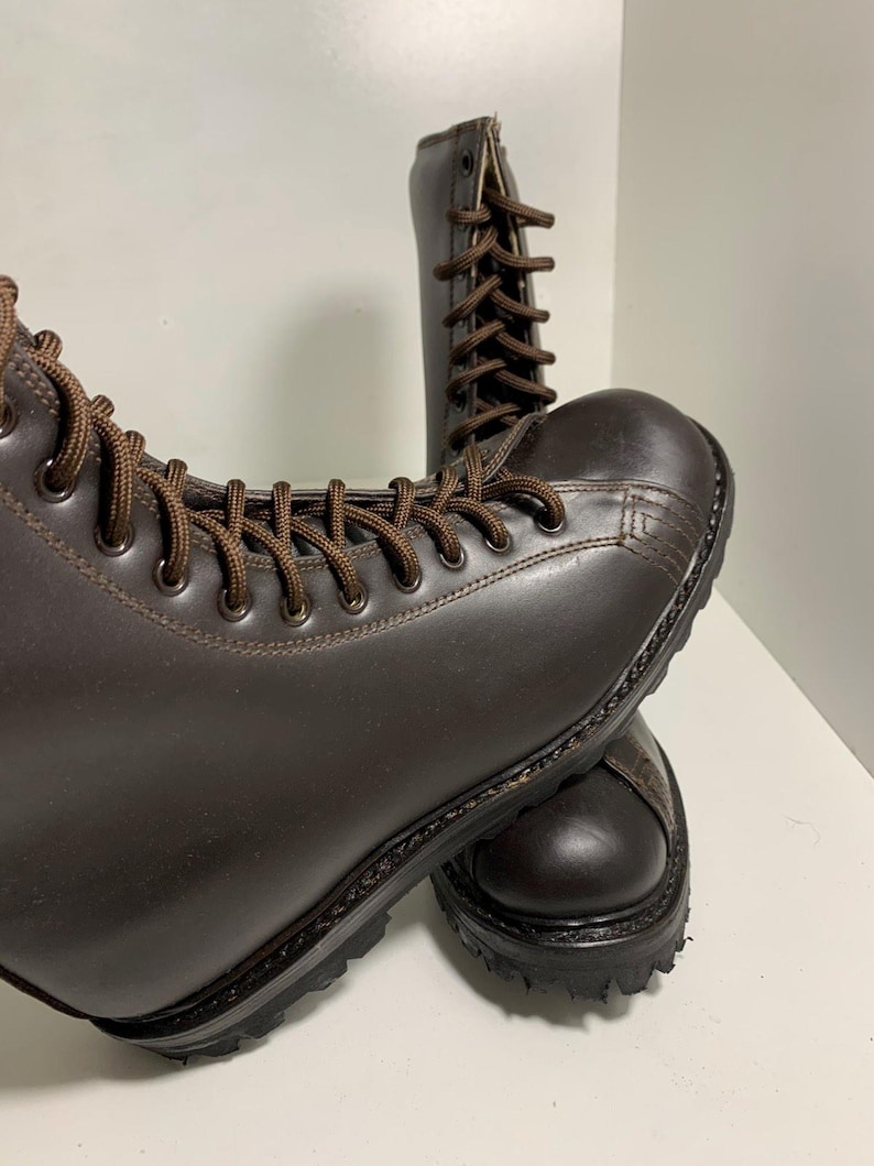 May include: A pair of brown leather boots with brown laces. The boots have a rounded toe and a thick, textured sole. The boots are laced up and appear to be new.