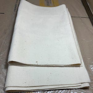 Puede incluir: Dos piezas de tela de algodón blanco dobladas juntas. La tela es lisa y tiene una superficie ligeramente texturizada.