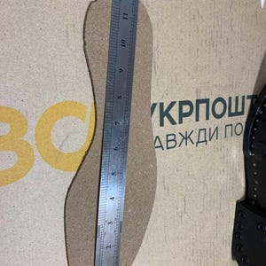 Puede incluir: Una plantilla de corcho se mide con una regla, mostrando una longitud de aproximadamente 30 cm. La plantilla es de color marr&oacute;n claro y tiene un dise&ntilde;o en forma de pie. La regla es plateada y tiene marcas en cent&iacute;metros. El fondo es una superficie marr&oacute;n claro con texto.