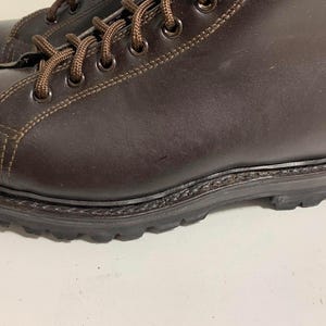 May include: Close-up of a pair of brown leather boots. The boots have brown laces, visible stitching, and a dark brown sole. The leather appears to be smooth and the boots are in good condition.