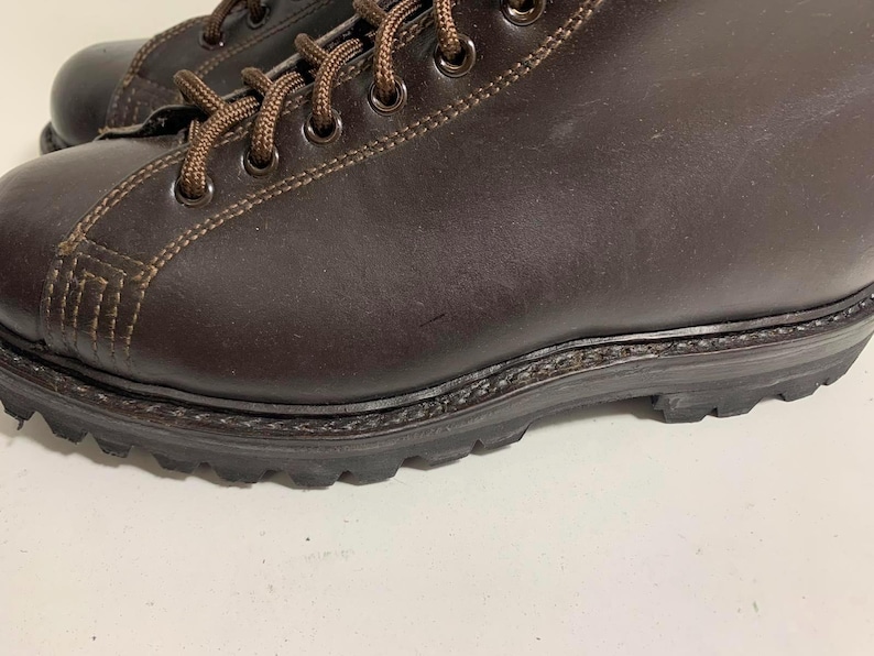 May include: Close-up of a pair of brown leather boots. The boots have brown laces, visible stitching, and a dark brown sole. The leather appears to be smooth and the boots are in good condition.