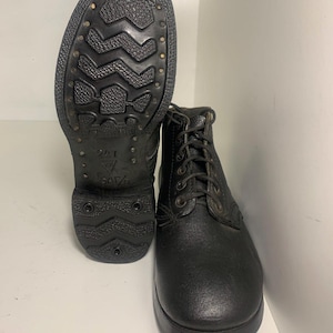 May include: A pair of black leather boots with a textured finish, featuring a lace-up front with metal eyelets and a thick, lugged rubber sole. The sole displays a prominent tread pattern and the embossed text 247 and SATRA on the heel area.