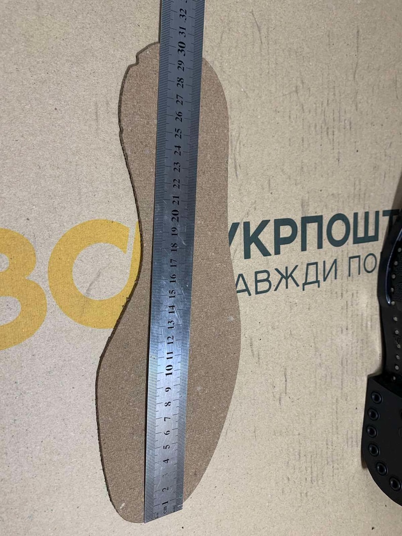 Puede incluir: Una plantilla de zapato de color beige se mide con una regla met&aacute;lica. La plantilla se coloca sobre una superficie marr&oacute;n claro. La regla muestra medidas en cent&iacute;metros. El texto "BC" y "КРПОШТ АВЖДИ ПО" son visibles.