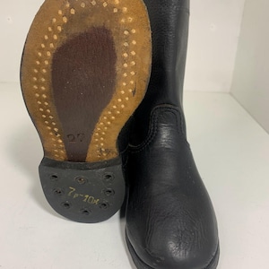 May include: Black leather riding boot with a worn, textured sole. The sole is brown with small, evenly spaced holes. The boot is tall, with a smooth, polished finish. The sole is marked with the size 7-10x.