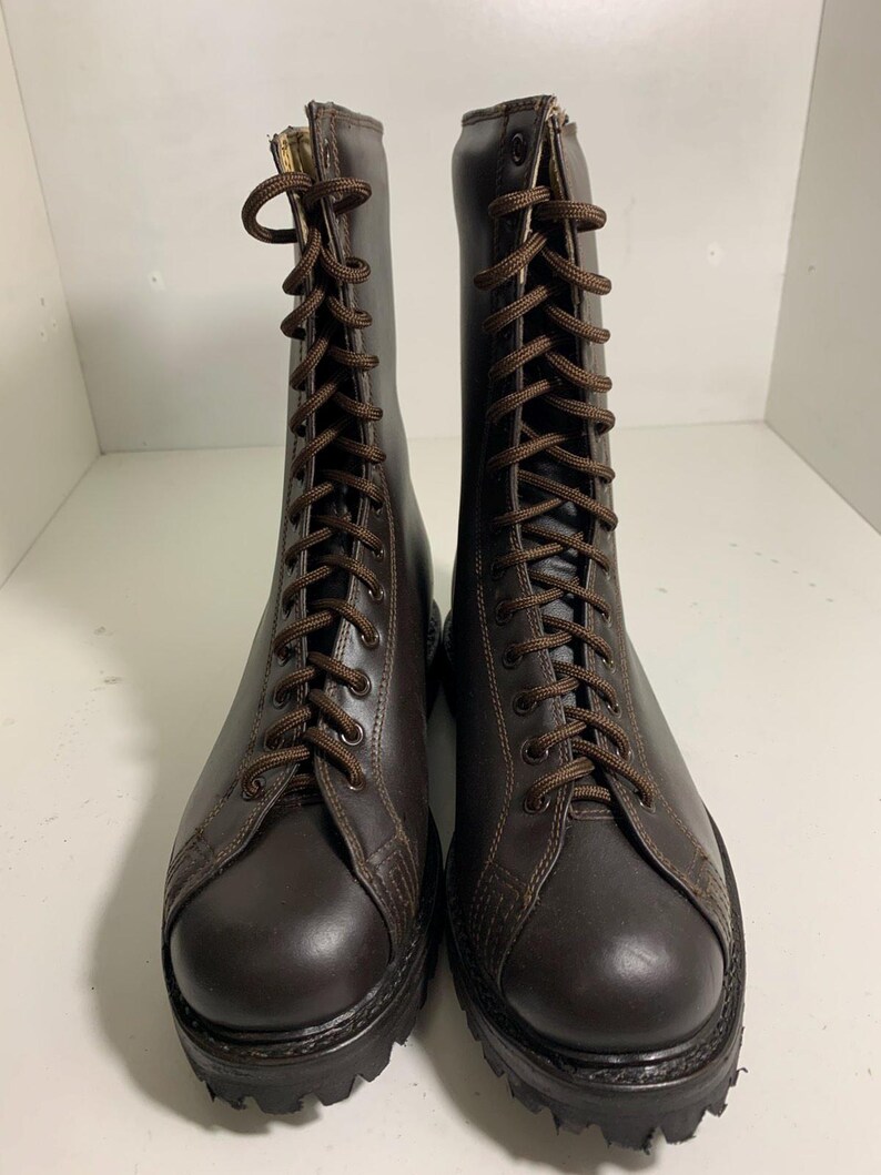 May include: A pair of brown leather combat boots with a lace-up design. The boots have a rounded toe, a thick sole, and brown laces. The boots are displayed on a white surface.