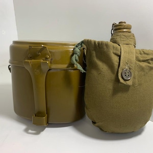 May include: An olive-drab metal canteen and a matching round container. The canteen is in a canvas pouch with a button closure. The container has a handle and a hinged lid. Both items appear to be vintage.
