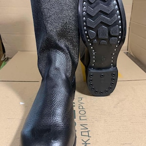 Puede incluir: Botas de cuero negro con acabado texturizado. Una bota est&aacute; de pie, la otra muestra la suela. Las botas tienen una ca&ntilde;a alta y una suela robusta, adecuadas para diversas condiciones. Las botas miden aproximadamente 30 cm de alto.