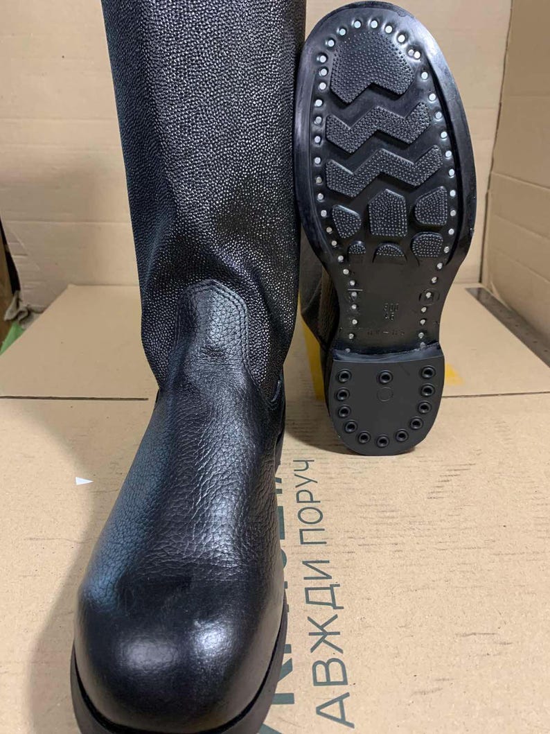 Puede incluir: Botas de cuero negro con acabado texturizado. Una bota est&aacute; de pie, la otra muestra la suela. Las botas tienen una ca&ntilde;a alta y una suela robusta, adecuadas para diversas condiciones. Las botas miden aproximadamente 30 cm de alto.