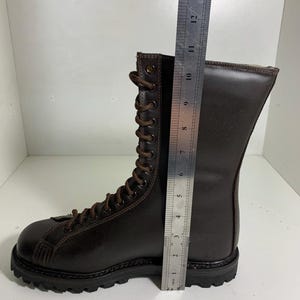 May include: A brown leather boot with a lace-up design. The boot is approximately 13 inches tall. The sole is black and rugged. The boot is made of a dark brown leather material.