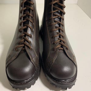 May include: A pair of brown leather combat boots with dark brown laces. The boots have a rounded toe and a thick, textured sole. The boots are laced up and appear to be new.