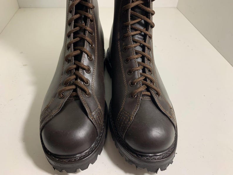 May include: A pair of brown leather combat boots with dark brown laces. The boots have a rounded toe and a thick, textured sole. The boots are laced up and appear to be new.