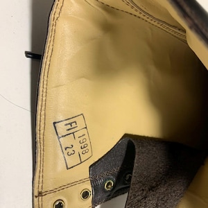 May include: Interior view of a brown leather boot. The boot's interior is tan with visible stitching and a stamped label. The label reads "FI 23 1998". The boot has brass eyelets and a dark brown leather exterior.