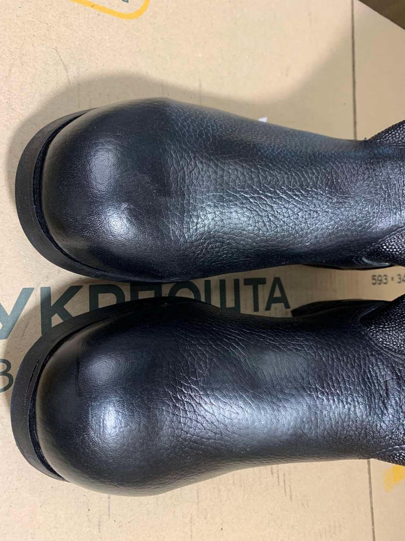 Puede incluir: Un par de botas de cuero negro con punteras redondeadas y empeines texturizados. Las botas tienen una suela oscura y un brillo sutil. Dise&ntilde;o sencillo y cl&aacute;sico.
