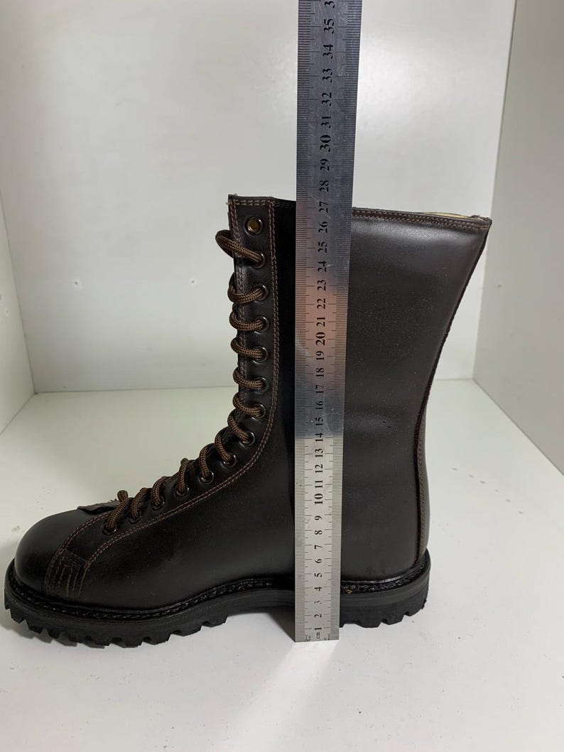 May include: A brown leather boot with a lace-up design. The boot measures approximately 11 inches in height. The sole is black and the laces are brown. The boot is on a white surface.