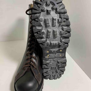 May include: A pair of black leather combat boots with brown laces and a thick, textured sole. The sole is made of dark gray rubber with metal studs. The boots are designed for durability and rugged use.