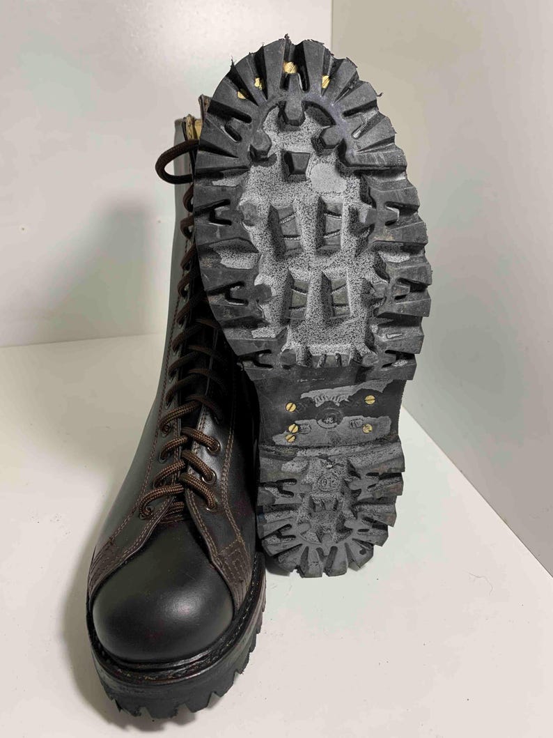 May include: A pair of black leather combat boots with brown laces and a thick, textured sole. The sole is made of dark gray rubber with metal studs. The boots are designed for durability and rugged use.