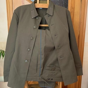May include: A dark green military uniform jacket and matching trousers with a blue trim. The jacket has a button fastening and multiple pockets.