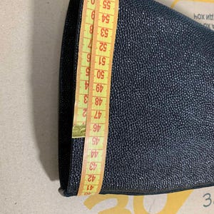 Puede incluir: Un objeto texturizado azul marino oscuro se mide con una cinta m&eacute;trica amarilla. La cinta muestra una medida de aproximadamente 40 a 59 cm. El objeto parece ser un trozo de tela o cuero.