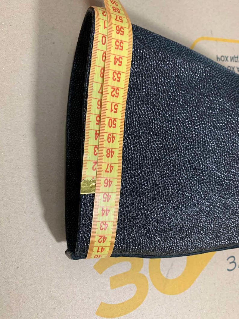 Puede incluir: Un objeto texturizado azul marino oscuro se mide con una cinta m&eacute;trica amarilla. La cinta muestra una medida de aproximadamente 40 a 59 cm. El objeto parece ser un trozo de tela o cuero.