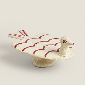 May include: A white ceramic dish shaped like a fish with red painted lines. The fish has a raised head and a small base.
