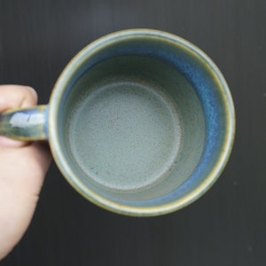 Puede incluir: Una taza de cer&aacute;mica hecha a mano con un esmalte azul y verde. La taza tiene una forma redondeada con un asa y una capacidad de aproximadamente 350 ml. El interior es de color verde claro y el borde es azul m&aacute;s oscuro.
