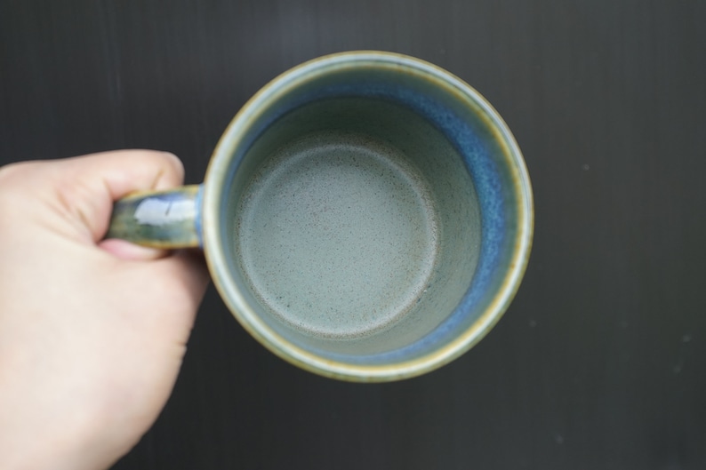 Puede incluir: Una taza de cer&aacute;mica hecha a mano con un esmalte azul y verde. La taza tiene una forma redondeada con un asa y una capacidad de aproximadamente 350 ml. El interior es de color verde claro y el borde es azul m&aacute;s oscuro.