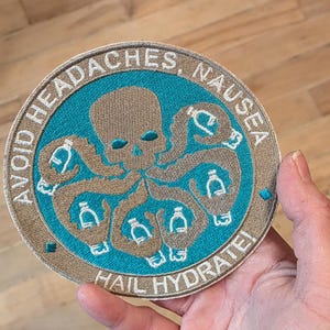 May include: Embroidered patch with a teal and brown design. The patch features an octopus-like skull with water bottles in its tentacles, surrounded by the text "AVOID HEADACHES, NAUSEA" and "HAIL HYDRATE!"