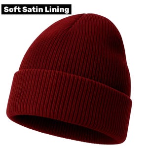 May include: A burgundy knit beanie with a folded brim. The hat has a ribbed texture and the text "Soft Satin Lining" in a white rectangle at the top. This warm hat is suitable for cold weather.