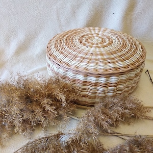 May include: A round woven storage basket with a white and brown striped pattern. The basket is made of natural materials and has a lid.