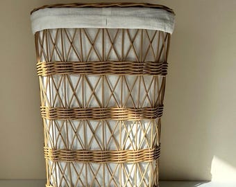 May include: A tall, rectangular laundry hamper made of woven rattan. The hamper features a light-colored, removable fabric liner and a woven lid. The exterior has a crisscross pattern and horizontal bands of woven material.