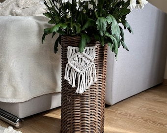 May include: A brown wicker vase with a white macrame hanging from the side. The vase is filled with white flowers.