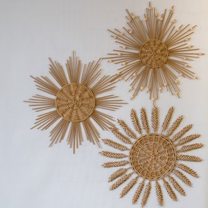 Pode incluir: Três peças de decoração de parede tecidas em forma de sol, com um círculo central e raios que irradiam. As peças são feitas de materiais naturais e têm uma estética rústica e boêmia.