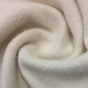 May include: Close-up of a soft, white fleece fabric. The fabric has a fuzzy texture and is folded in a way that shows its texture.