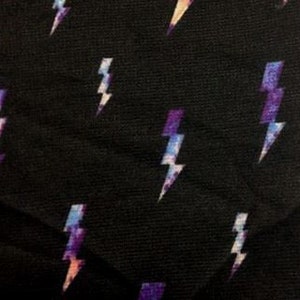 May include: Black fabric with a repeating pattern of purple, blue, and pink lightning bolts.