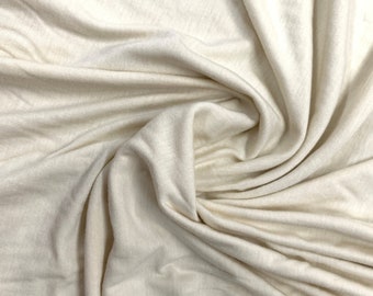 May include: A close-up of a soft, cream-colored fabric with a smooth texture. The fabric is draped and folded, creating a flowing and elegant look.