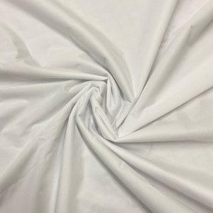 May include: White fabric with a smooth, silky texture. The fabric is folded and draped, creating soft folds and curves.