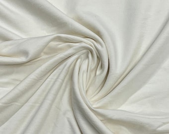 May include: A close-up of a smooth, off-white fabric with a soft, drapey texture. The fabric is folded and bunched, creating a sense of movement and flow.
