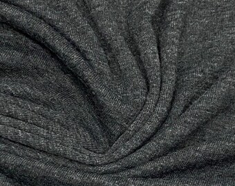 May include: Close-up of a dark gray fabric with a textured, knitted surface. The fabric is folded and draped, showing its soft and flexible texture.