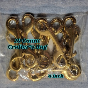 May include: A bag of 10 gold-toned metal trigger snap clasps, each measuring 1 inch in length. The bag has a label that reads "10 Count Crafter's Bag 1 inch".
