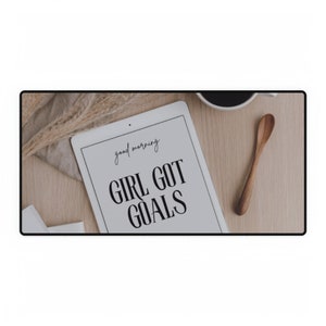 Puede incluir: Una tableta blanca con el texto "good morning" y "GIRL GOT GOALS" sobre una superficie de madera con una taza de café y una cuchara de madera.